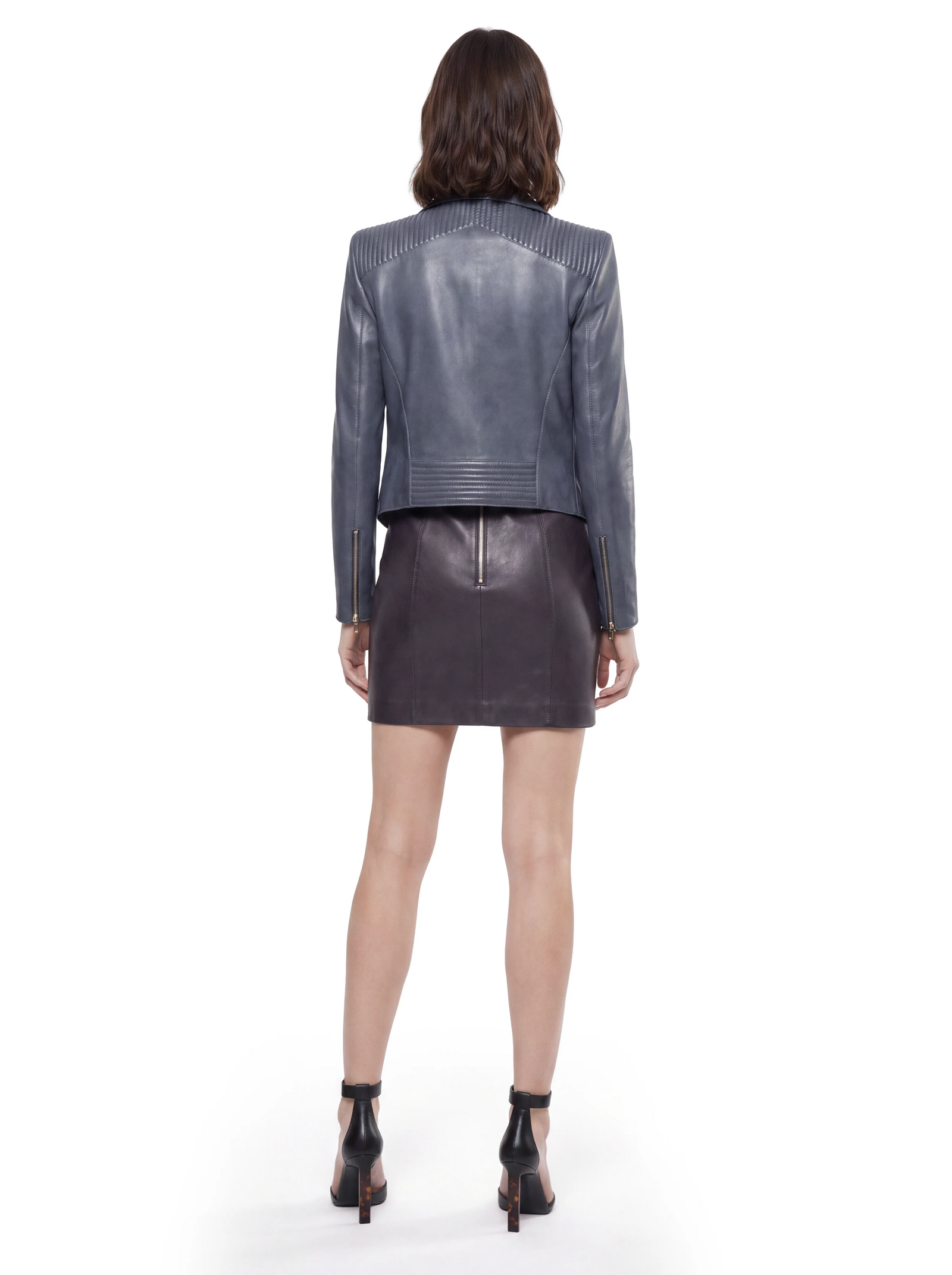 Graue Luxus Designer Lederjacke in der Rückansicht mit markanten Steppdetails im Schulterbereich und am unteren Rücken. Die klare Nahtführung, taillierte Silhouette und goldfarbenen Reißverschlüsse an den Ärmelabschlüssen unterstreichen den modernen, hochwertigen Charakter.